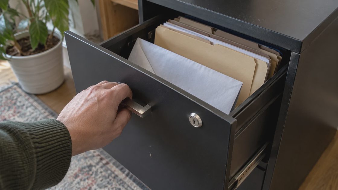 Online Document Vault: Maintenance record A hand closing a filing drawer containing organized paper folders.